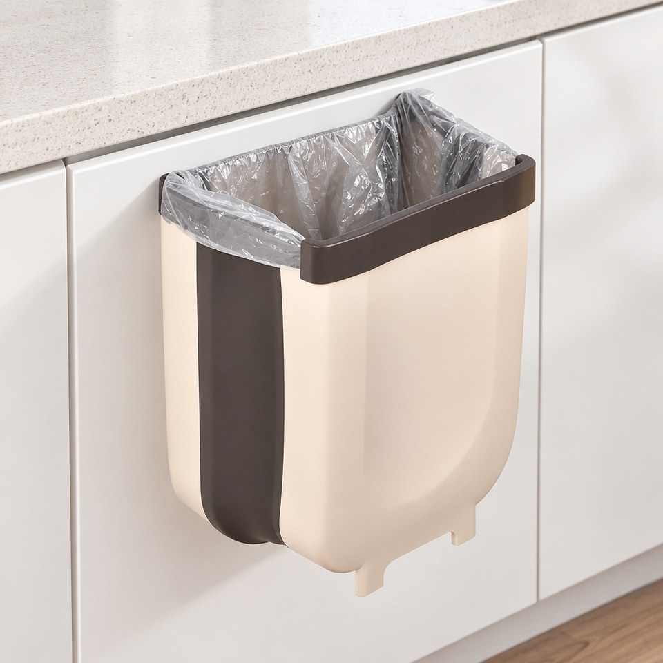 Basurero plegable beige colgado del borde de la puerta de un mueble de cocina, con una bolsa transparente en el aro