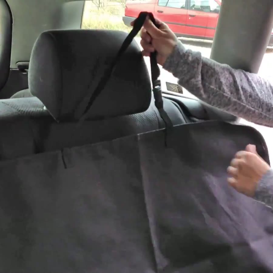 Detalle de la correa negra de un cubre asiento para mascotas pasada por el apoyacabezas trasero de un auto
