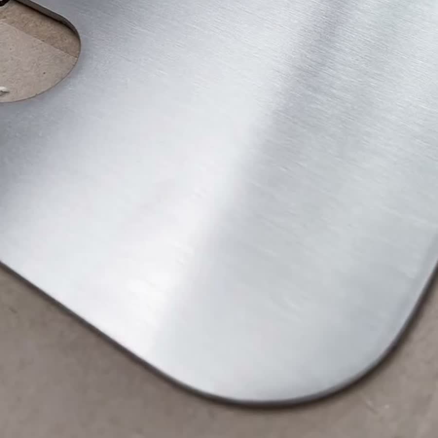 Detalle de la esquina de una tabla de picar de acero inoxidable cepillado, con la ranura para sujetarla